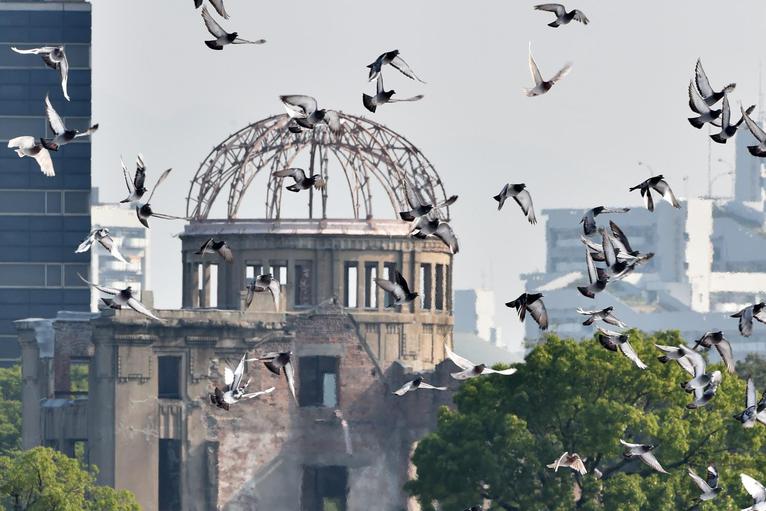 Palomas que sobrevuelan el Parque Conmemorativo de la Paz en Hiroshima con la llamada "Cúpula de la Bomba Atómica" en primer plano.